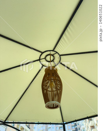 Light fixture hangs from the center of a large outdoor umbrella on a sunny day in a city, providing illumination for people below Light fixture hangs from the center of a large outdoor umbrella on a sunny day in a city, providing illumination for people below 140651022