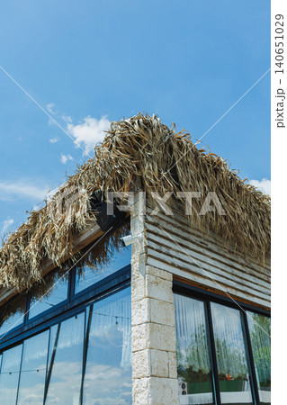 Peaceful eco retreat. Sunlit corner featuring reflective glass and straw textures. Contemporary structure under blue sky with sustainable design elements in view 140651029
