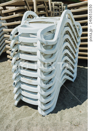 Outdoor yard features layered white loungers with curved designs. Resort area displays horizontally stacked white sunbeds on gravel with repetitive curved structures Outdoor yard features layered white loungers with curved designs. Resort area displays horizontally stacked white sunbeds on gravel with repetitive curved structures 140651030