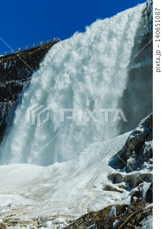 Niagara Falls shows water rushing down rocks with ice and snow nearby in clear blue sky during winter months in North America Niagara Falls shows water rushing down rocks with ice and snow nearby in clear blue sky during winter months in North America 140651087