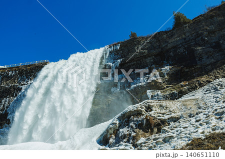 Niagara Falls shows water rushing down frozen rocks with clear sky overhead during winter season 140651110