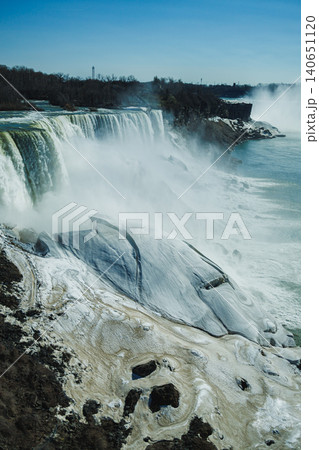 Water flows over cliffs at Niagara Falls during a sunny day in spring with mist rising from the waterfalls and rocks nearby Water flows over cliffs at Niagara Falls during a sunny day in spring with mist rising from the waterfalls and rocks nearby 140651120