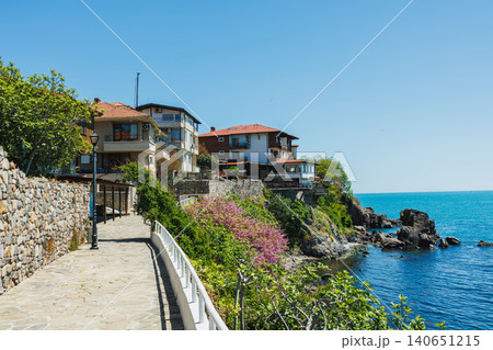 Sunny seaside stroll. Coastal path with scenic views. Serene seaside walkway overlooking rocky cliffs. Bright coastal trail alongside vibrant bougainvillea and calm waters Sunny seaside stroll. Coastal path with scenic views. Serene seaside walkway overlooking rocky cliffs. Bright coastal trail alongside vibrant bougainvillea and calm waters 140651215