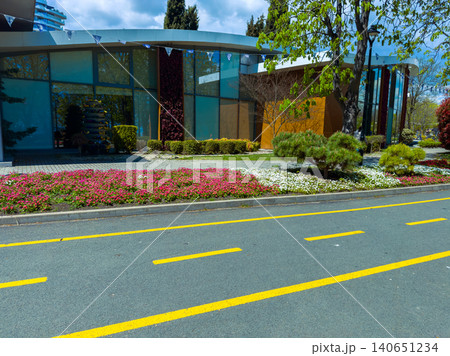 Flowers line the pathway beside a modern building in a city with trees and blue skies during daytime Flowers line the pathway beside a modern building in a city with trees and blue skies during daytime 140651234