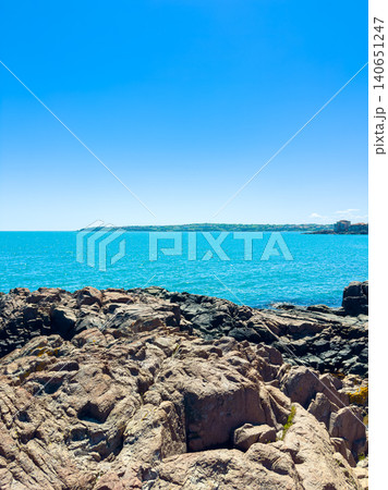 People explore rocky coastline near blue ocean on a sunny day with clear sky People explore rocky coastline near blue ocean on a sunny day with clear sky 140651247