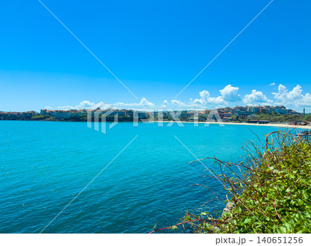 Bright day at the coastal town with clear water and distant hills showcasing buildings along the shore Bright day at the coastal town with clear water and distant hills showcasing buildings along the shore 140651256