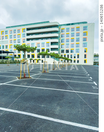 Empty parking lot with young trees in front of a large modern building on a cloudy day in an urban area Empty parking lot with young trees in front of a large modern building on a cloudy day in an urban area 140651286