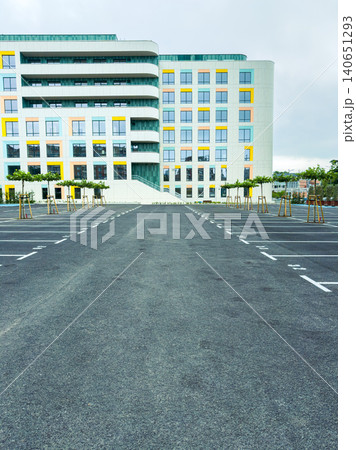 Empty parking lot in front of a modern building during a cloudy day with few trees lined along the sides Empty parking lot in front of a modern building during a cloudy day with few trees lined along the sides 140651293