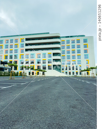 Modern building with colorful windows and empty parking lot during cloudy weather in an urban area Modern building with colorful windows and empty parking lot during cloudy weather in an urban area 140651296