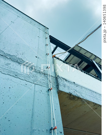 Building construction shows blue concrete wall with white cables leading to upper structure under cloudy sky Building construction shows blue concrete wall with white cables leading to upper structure under cloudy sky 140651398