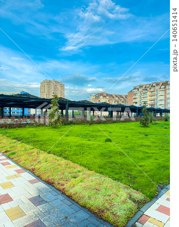Green grass and buildings under blue sky in urban park setting during daytime with clouds in the background Green grass and buildings under blue sky in urban park setting during daytime with clouds in the background 140651414