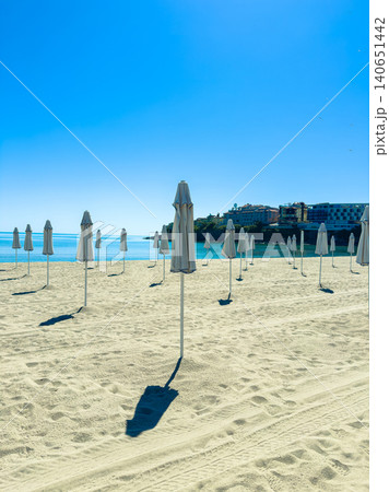 Sunny beach with empty umbrellas standing in sand during mid-morning near the ocean at a popular seaside location Sunny beach with empty umbrellas standing in sand during mid-morning near the ocean at a popular seaside location 140651442