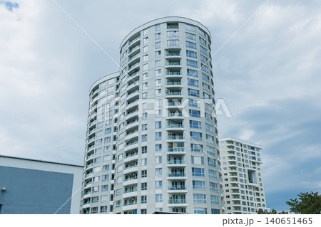 Tall residential buildings stand under a cloudy sky in a city as people walk on the street below during the day Tall residential buildings stand under a cloudy sky in a city as people walk on the street below during the day 140651465