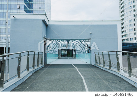Modern walkway connects buildings in urban area, showcasing glass architecture and smooth pavement during cloudy day 140651466