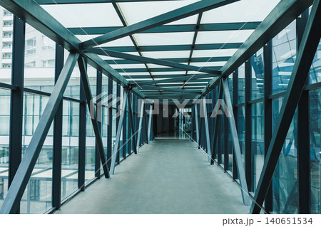 Modern walkway connects buildings in urban area during daytime showing clear glass walls and metal frames Modern walkway connects buildings in urban area during daytime showing clear glass walls and metal frames 140651534