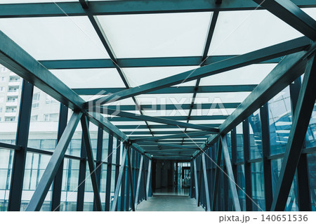 Bridge connects two buildings at a modern structure with glass walls and metal framework, taken during daytime showing clear sky Bridge connects two buildings at a modern structure with glass walls and metal framework, taken during daytime showing clear sky 140651536