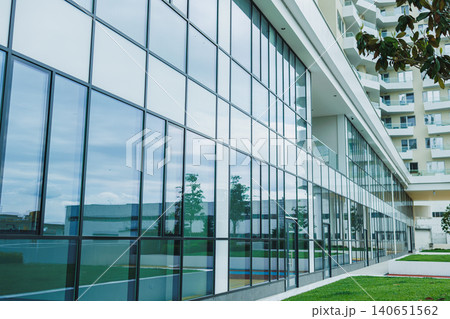 Modern building with large glass windows reflecting clouds and nearby structures under a cloudy sky in an urban area during the day 140651562