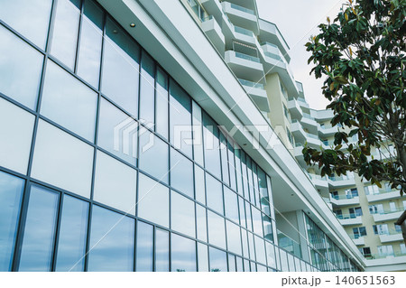 Modern building with large glass windows in a city landscape during the day showing reflections of the sky and surrounding structures 140651563