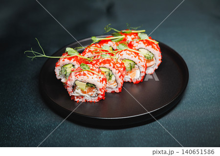 Fresh sushi rolls prepared with crab, cucumber, and avocado on a black plate at a modern kitchen setting during the day 140651586