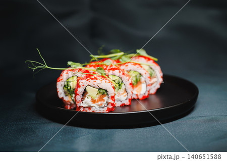Sushi rolls with cucumber and crab on black plate served on dark background during dinner time Sushi rolls with cucumber and crab on black plate served on dark background during dinner time 140651588