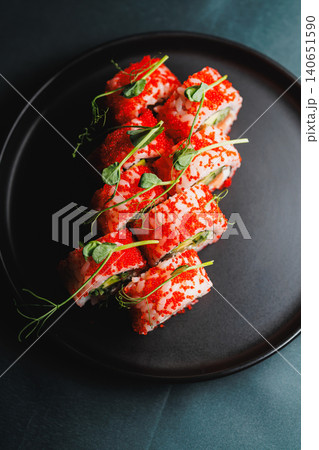 Sushi rolls with red roe and greens served on a black plate in a restaurant setting during lunch hour 140651590