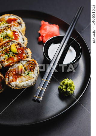 Sushi rolls served on a black plate with chopsticks and garnishes in a dining setting during dinner time 140651618