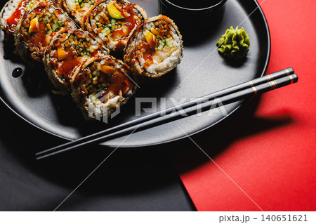 Fresh sushi rolls served on a black plate with chopsticks and wasabi on a red and black background during a dining experience Fresh sushi rolls served on a black plate with chopsticks and wasabi on a red and black background during a dining experience 140651621