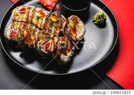 Sushi rolls on a black plate with sauce, wasabi, and pickled ginger, placed on a red tablecloth during a lunch meal in a restaurant setting 140651623