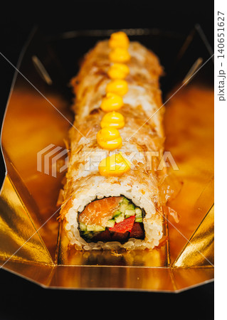 Sushi roll with vegetables, fish, and sauce served in a gold box in a restaurant setting during dinner time 140651627