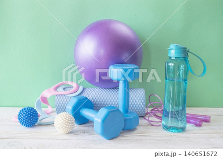 Fitness equipment for home workouts on wooden floor. Yoga and Pilates fitness equipment with dumbbells, yoga ball, massage roller, resistance bands and water bottle. Fitness equipment for home workouts on wooden floor. Yoga and Pilates fitness equipment with dumbbells, yoga ball, massage roller, resistance bands and water bottle. 140651672