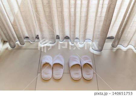 Top view of white slippers by white sheer curtains and soft sunlight, vacation concept Top view of white slippers by white sheer curtains and soft sunlight, vacation concept 140651753