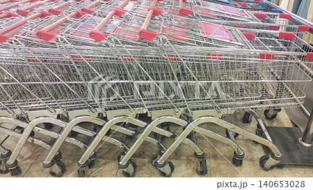 Metal shopping trolleys with red handles stacked in a retail store. 140653028