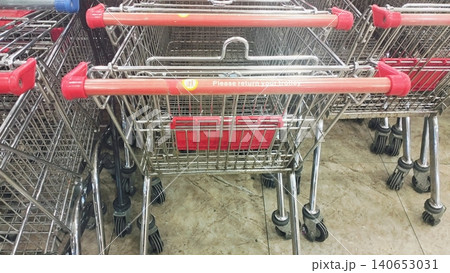 Metal shopping trolleys with red handles stacked in a retail store. Metal shopping trolleys with red handles stacked in a retail store. 140653031