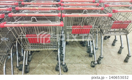 Metal shopping trolleys with red handles stacked in a retail store. 140653032