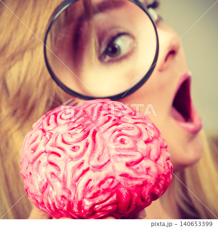 Woman holding magnifying glass investigating brain Woman holding magnifying glass investigating brain 140653399