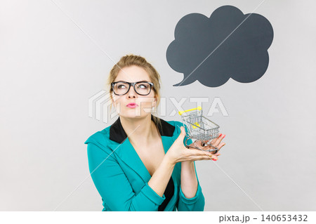 Thinking business woman holding small tiny shopping cart Thinking business woman holding small tiny shopping cart 140653432