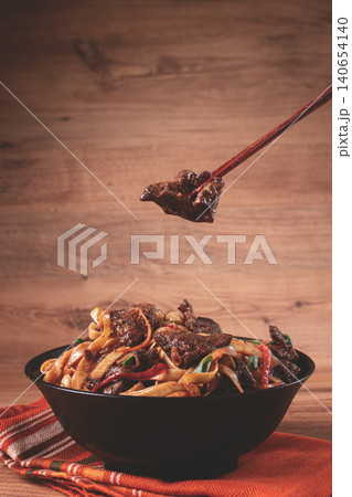 Udon noodles with beef in Mongolian style, with green onions and vegetables, homemade, on a wooden table, 140654140