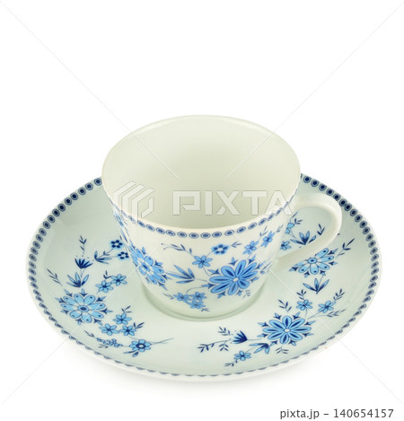 Elegant ceramic tea cup with a matching saucer featuring classic blue floral ornaments, isolated on a clean white background in a high angle square frame studio shot. 140654157