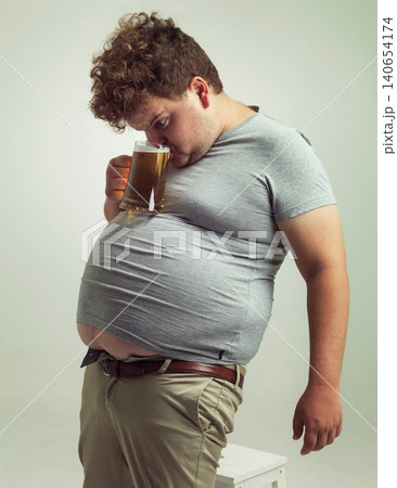 Obese, weight gain and alcohol for man in studio with drink for unhealthy habit, plus size and joke. Overweight person with glass on fat stomach for balance, comedy and humor for lager and comic 140654174