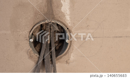 Cables Emerging From Circular Junction Box, Insulation Stripped And Conductors Visible, Rough Plaster Edge, Close Viewpoint Revealing Core Electrical Components And Prep Work Cables Emerging From Circular Junction Box, Insulation Stripped And Conductors Visible, Rough Plaster Edge, Close Viewpoint Revealing Core Electrical Components And Prep Work 140655683