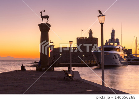 Sunrise view of Mandraki Harbor with Saint Nicholas Fortress, deer monument and luxury yacht in Rhodes, Greece. Sunrise view of Mandraki Harbor with Saint Nicholas Fortress, deer monument and luxury yacht in Rhodes, Greece. 140656269