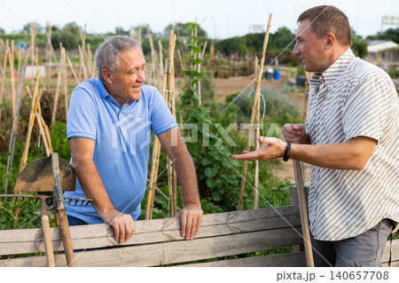 Two male farmers talking outside next to wooden fence on background with farm 140657708