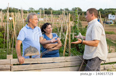 Quarrel of neighbors in country in village. Elderly couple and neighbor are in conflict near wooden fence Quarrel of neighbors in country in village. Elderly couple and neighbor are in conflict near wooden fence 140657729