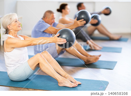 Sitting on mat mature woman instructor conducts training with fitball for group students. Sitting on mat mature woman instructor conducts training with fitball for group students. 140658108