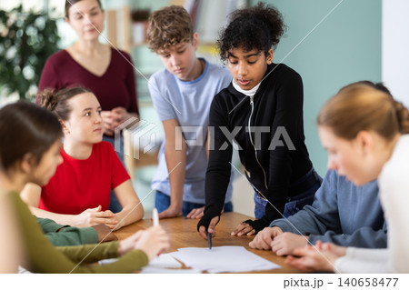 Group of teenagers and students discuss the task at the table in classroom Group of teenagers and students discuss the task at the table in classroom 140658477