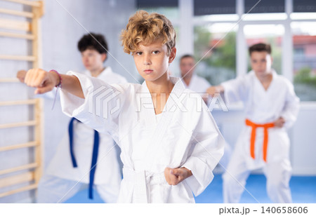 Preteen attendee of karate classes practicing kata standing in row with others Preteen attendee of karate classes practicing kata standing in row with others 140658606