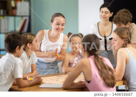 Children and teenagers playing board game at table with teacher nearby Children and teenagers playing board game at table with teacher nearby 140658887