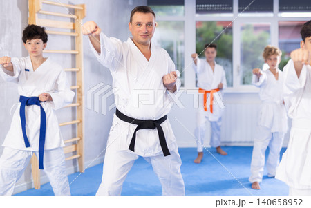 Teenagers in kimonos practicing effective karate techniques in group workout with their trainer in foreground at training room 140658952