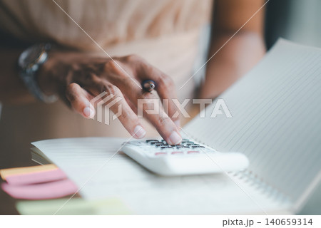 Closeup of hands pressing calculator on lined notebook with sticky notes, representing budget planning, accounting workflow, financial calculation, expense tracking, data review, and organization. 140659314