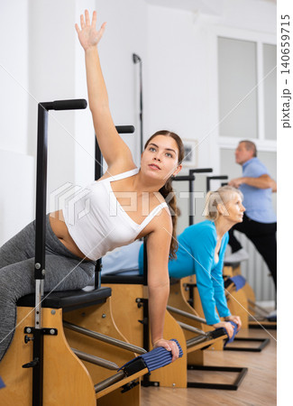 Positive young woman doing Pilates sitting exercise on Wanda chair in fitness center 140659715